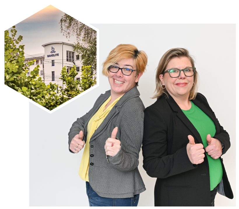 Two individuals standing back-to-back, both giving thumbs-up gestures. Their faces are blurred for privacy. The person on the left wears a grey blazer over a yellow top, and the person on the right wears a black blazer over a green top. In the upper left corner, there is a hexagonal inset photo of a building labeled 'Bakelite,' partially obscured by trees.